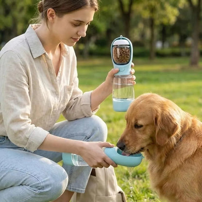 Woman feeding a dog from a portable pet water and food dispenser in a park.