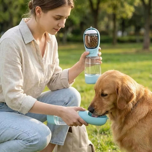Woman feeding a dog from a portable pet water and food dispenser in a park.