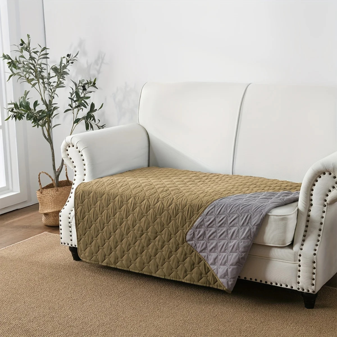 White sofa with beige quilted cover and gray blanket in a living room setting.